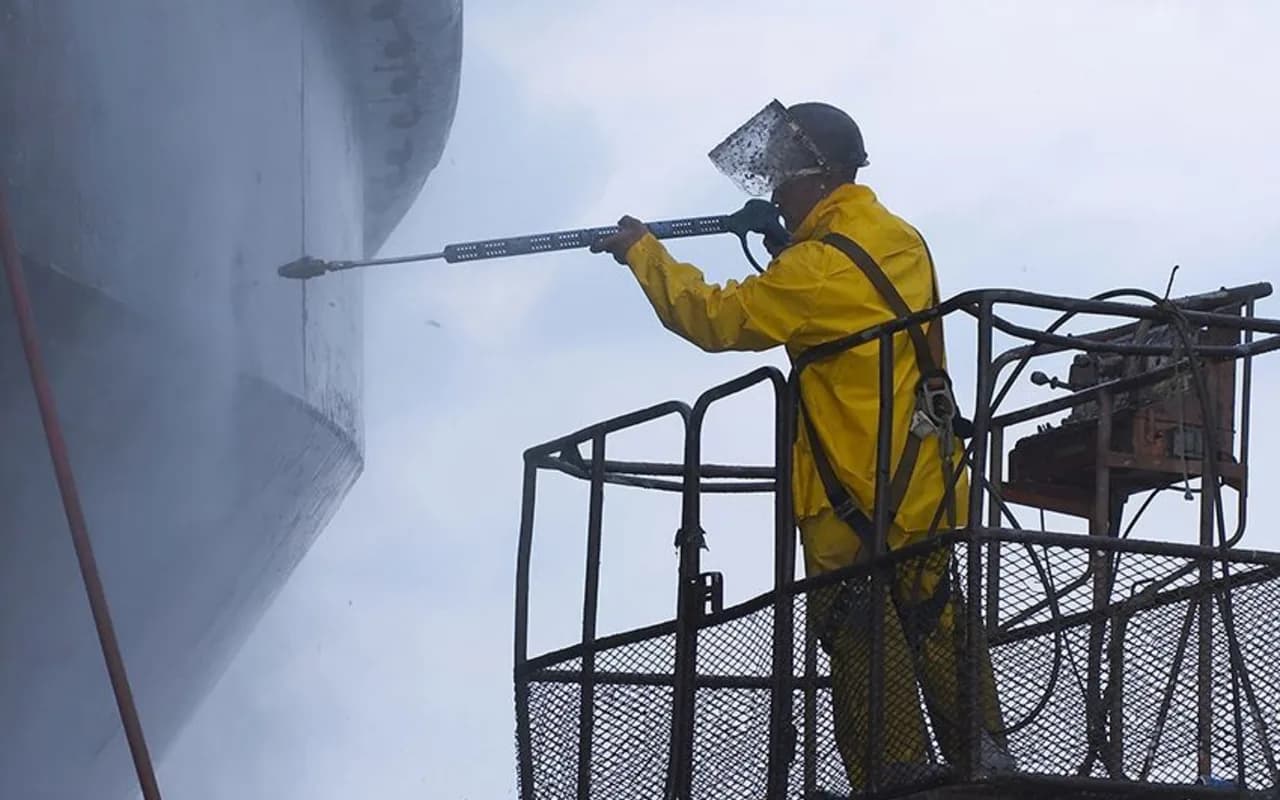 Nettoyage industriel en hauteur depuis une nacelle élévatrice, opérateur équipé d'un EPI complet.